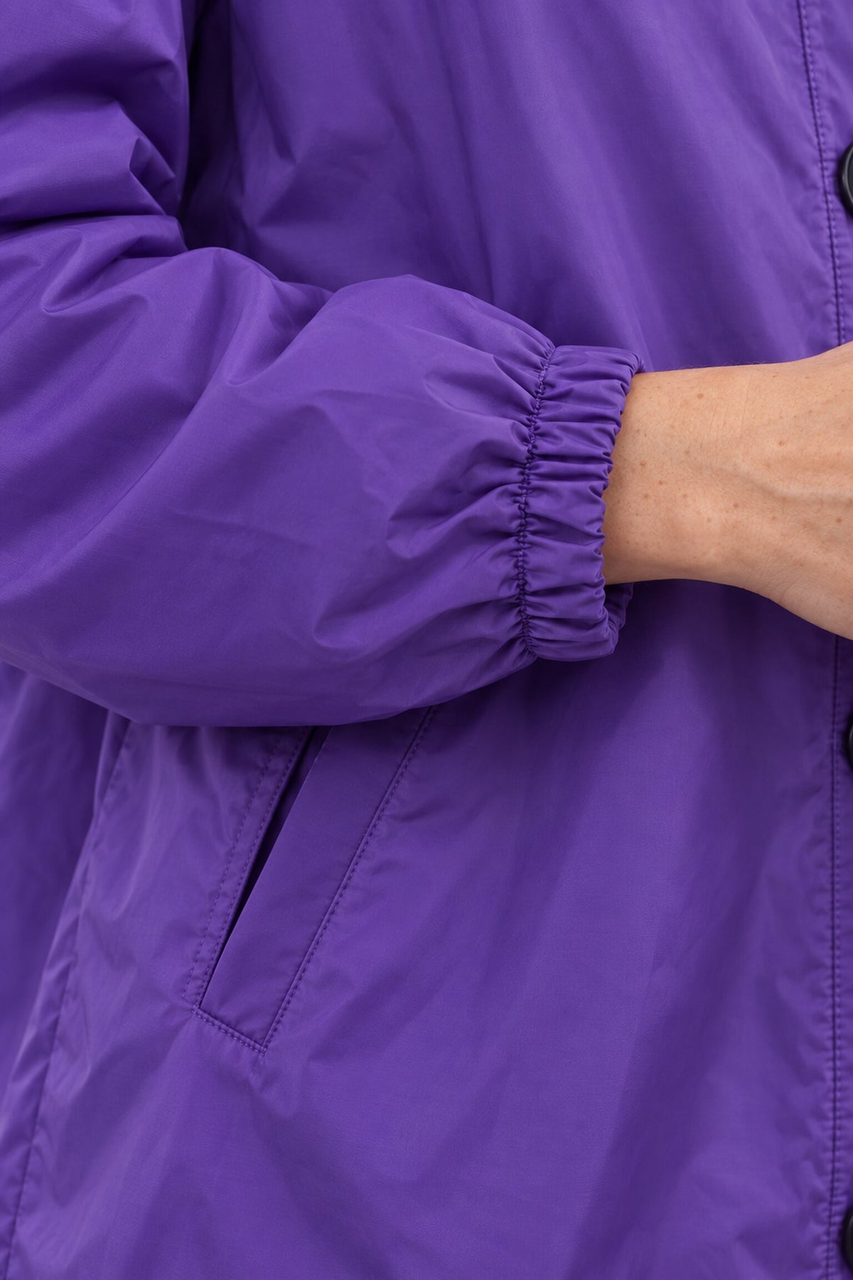 A person wears a purple Icon Milano Windbreaker Rain Jacket featuring elastic cuffs. Their hand is partially visible near the jacket opening, and a side pocket is shown on the left side of this water-resistant jacket.