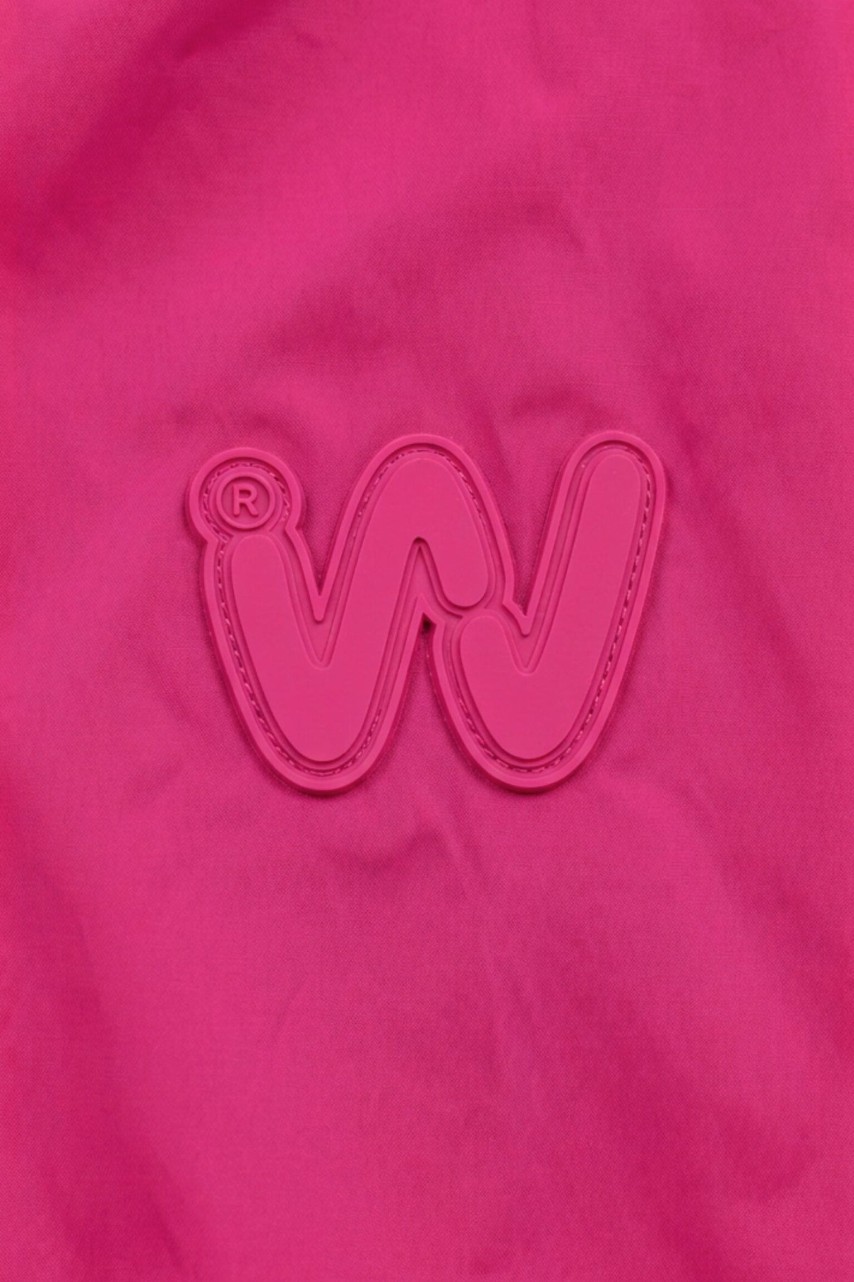 A pink fabric background features a raised, embroidered “W” logo and a subtle registered trademark symbol in the top left, both in a slightly deeper shade of pink—mirroring the refined elegance of Italian-designed women’s outerwear like the Icon Milano Windbreaker Rain Jacket.