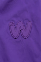 A raised, stylized “W” logo with a registered trademark symbol appears on a solid purple fabric background, evoking the signature look of the Icon Milano Windbreaker Rain Jacket.