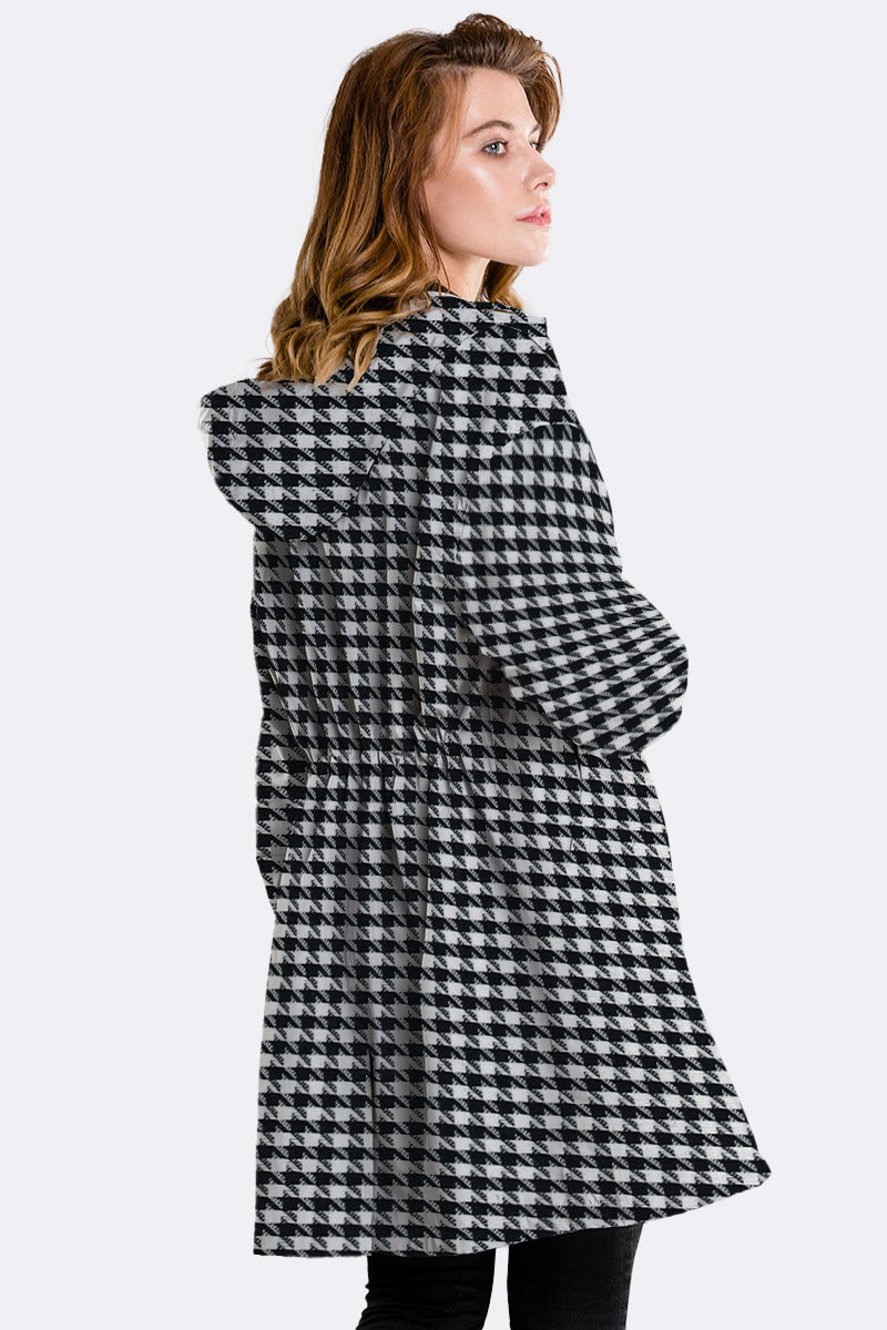 A woman with light brown hair wears the looselyboho HOUNDSTOOTH WINDBREAKER with a hood, turned slightly to the side and looking over her shoulder against a plain light background.