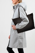 A person in a light gray hooded raincoat and black leggings carries the Free Gift Urban Slate Waterproof bag, ideal for smart organization. The background is plain white.