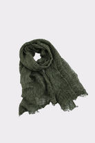 The Lightweight Linen Scarf, in dark green linen, lies flat on a light grey background with one end rolled and slightly frayed edges—an ultra-breathable, versatile accessory for any season.
