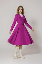 A woman with wavy hair and a neutral expression stands against a plain background wearing the looselyboho Water-Repellent Rain & Shine A-Line Hooded Raincoat in bright magenta, styled with white chunky knee-high boots.